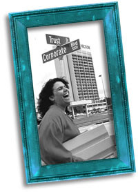 Black and white photograph of Judith Helfand laughing at an intersection marked "Trust" and "Corporate". 