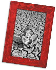 Black and white photograph of a boy sitting on dry, cracked ground. 