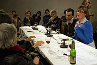 Photo of several people seated at a long table, some drinking wine.