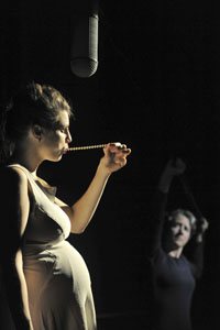 Photo of a pregnant woman on stage, pulling a string of pearls out of her mouth.
